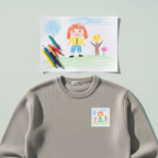 Grey kids sweatshirt with a child's crayon drawing printed on the chest, drawing and crayons above